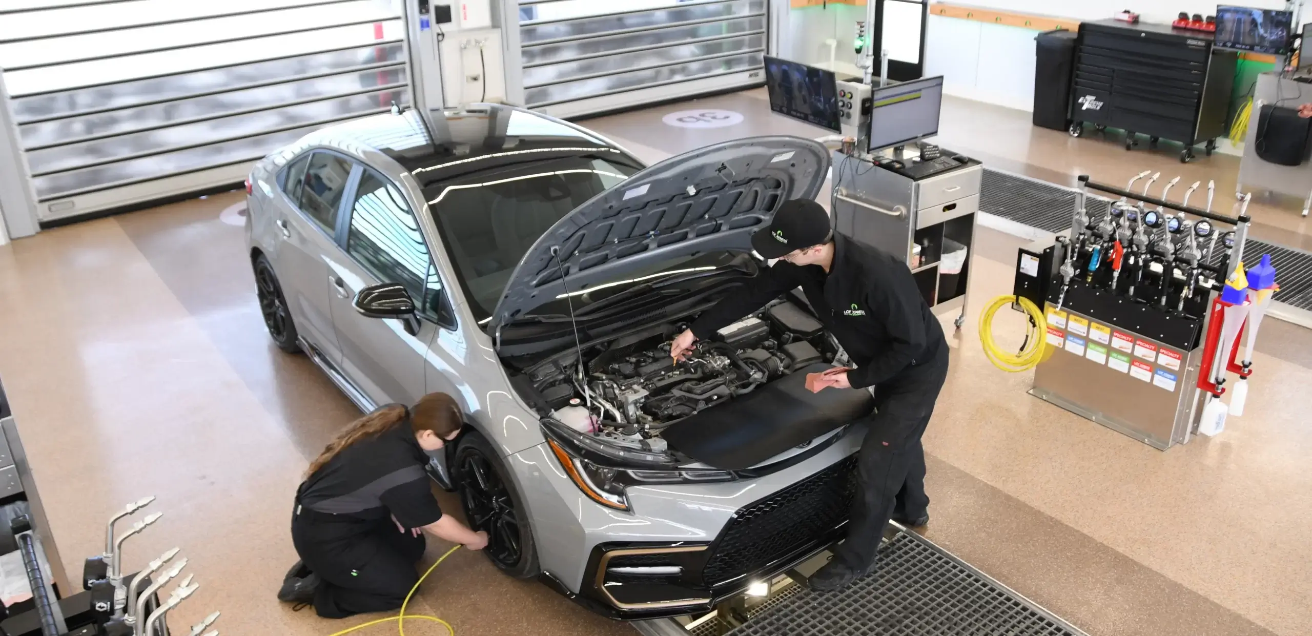 two LOF Xpress employees work on silver SUV, one on the wheel and the other opening the front hood