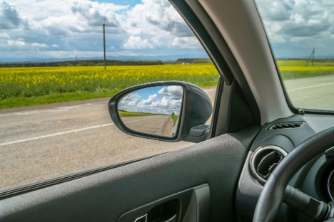A picture of a mirror on a car with the reflection of a road